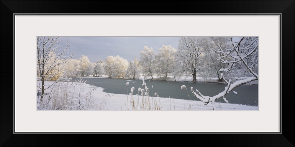 A frozen lake is photographed and surrounded by snow covered trees and land.