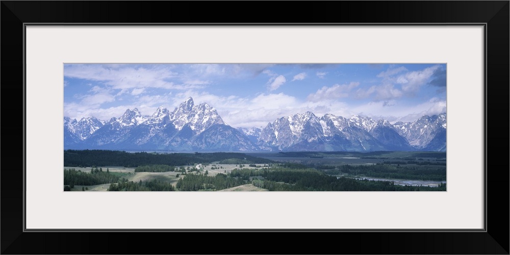 Panoramic picture taken of an immense mountain range in Wyoming. Vast terrain covered with trees lays in front of the snow...