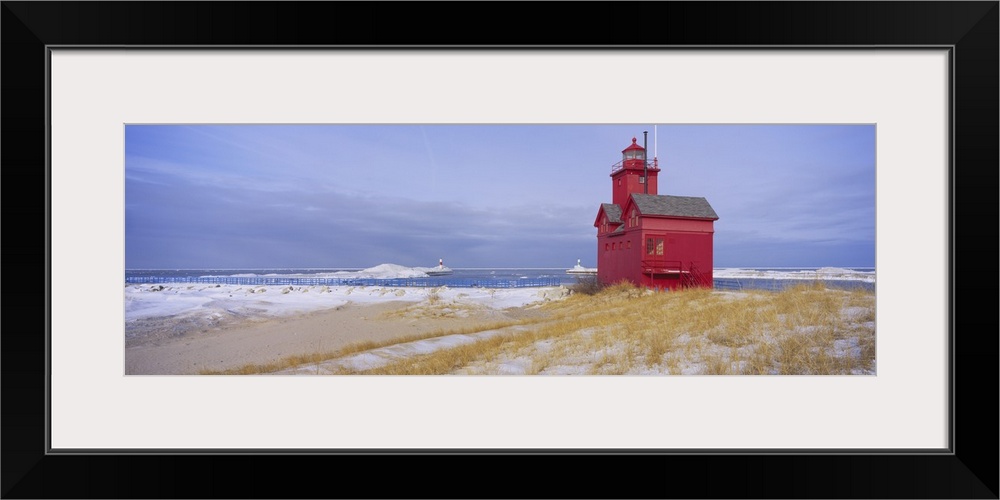 Lonely red light house on the edge of the water on a snowy beach, standing out against the pale cloudy sky.