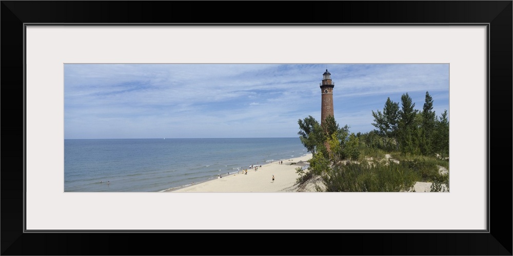 A light house on a sandy shore obscured by costal plant life and a partially cloudy sky.