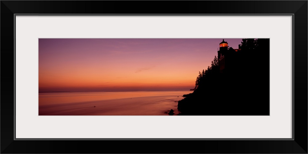 Panoramic photograph taken during a sunset with a lighthouse shown on the right side of the picture atop a hill that is si...