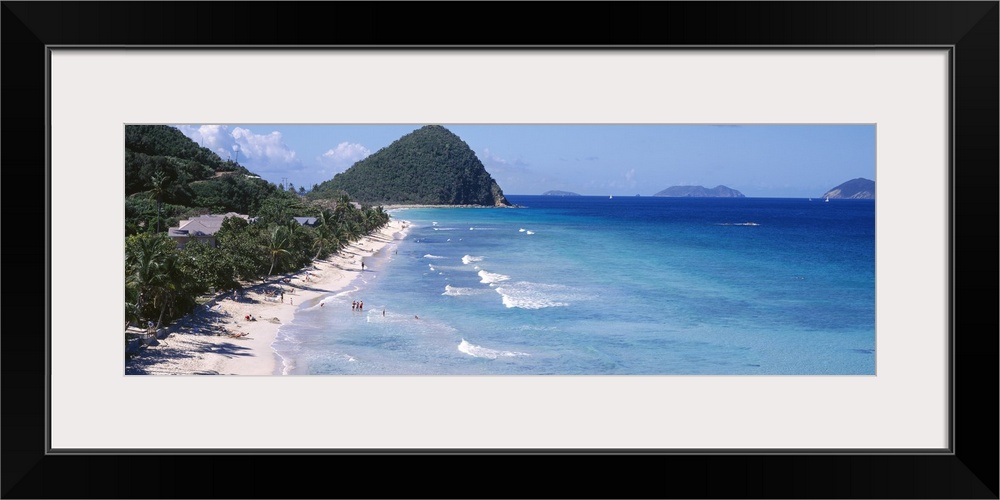 Panoramic photo of an ocean meeting a white sand beach with tropical vegetation.