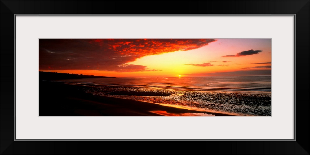 This is a panoramic photograph a flat sandy beach and sunset.