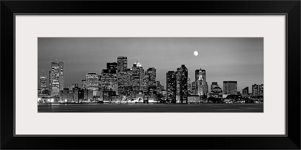 A panoramic of the skyscrapers in Boston lit up at night and the moon above the city.