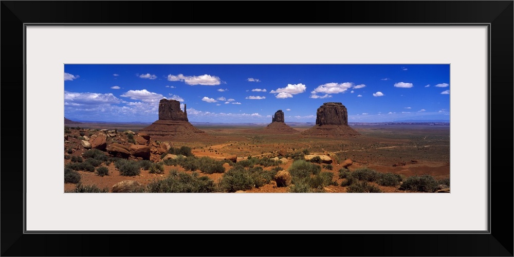 Panoramic photo on canvas of three tall rock formations in the desert under a bright blue sky.