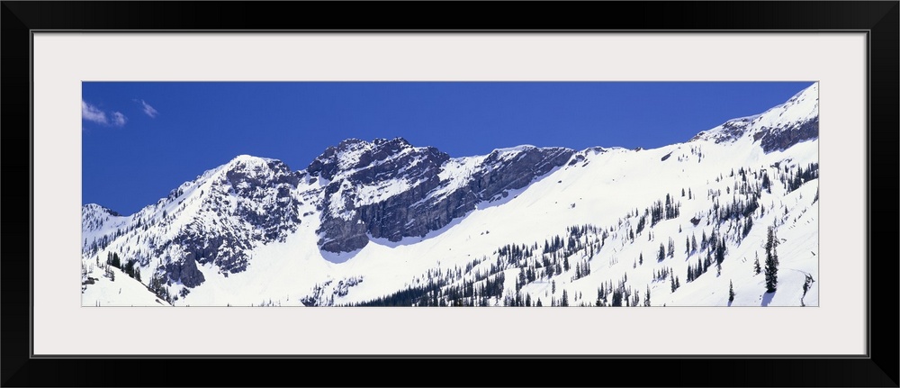 Wide angle photograph of snow covered mountains of Little Cottonwood Canyon, beneath a bright blue sky, in Salt Lake City,...