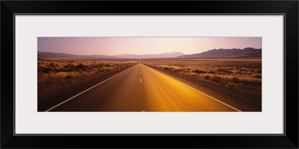 Long horizontal canvas photo of a long two lane road going straight into the distance of a desert landscape.