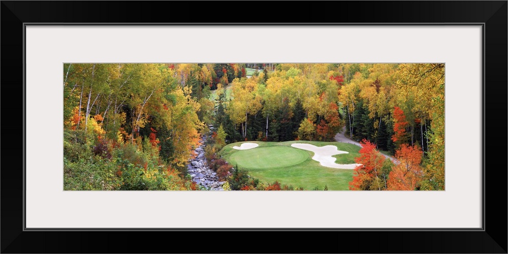 View over the forest canopy of a golf course and sand traps in a clearing surrounded by trees in fall colors.