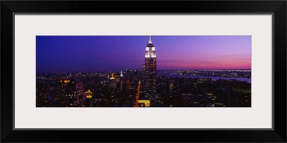 This is a panoramic photograph of the Manhattan skyline at night contrasting with a dramatic and vibrantly hued sky.