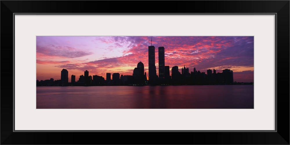 Dramatic photograph of the New York City skyline at sunset, with the World Trade Center towers silhouetted against a sky f...