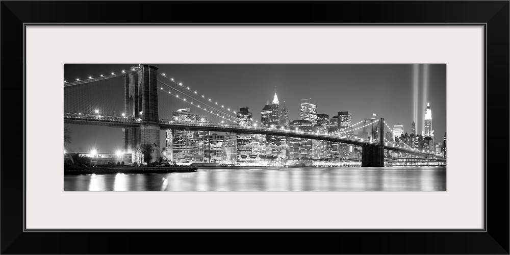 A panoramic landscape photo taken after 2001 of Manhattan and Brooklyn Bridge shining bright over the East River at night.