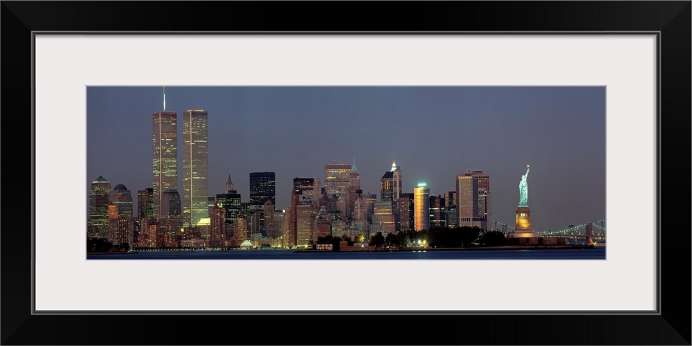 Panoramic photograph of the New York skyline at night, with the Twin Towers and the Statue of Liberty on a large wall hang...