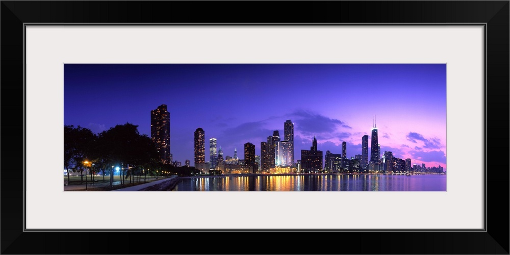 A panoramic of the Chicago cityscape lit up at dusk and reflecting on Lake Michigan.