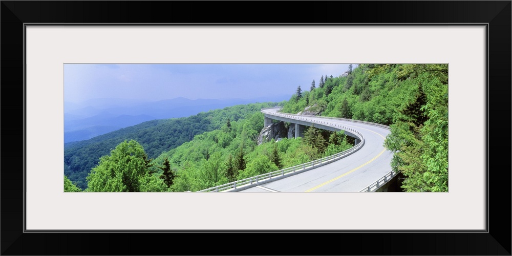 Panoramic photograph of road winding through tree covered mountains.