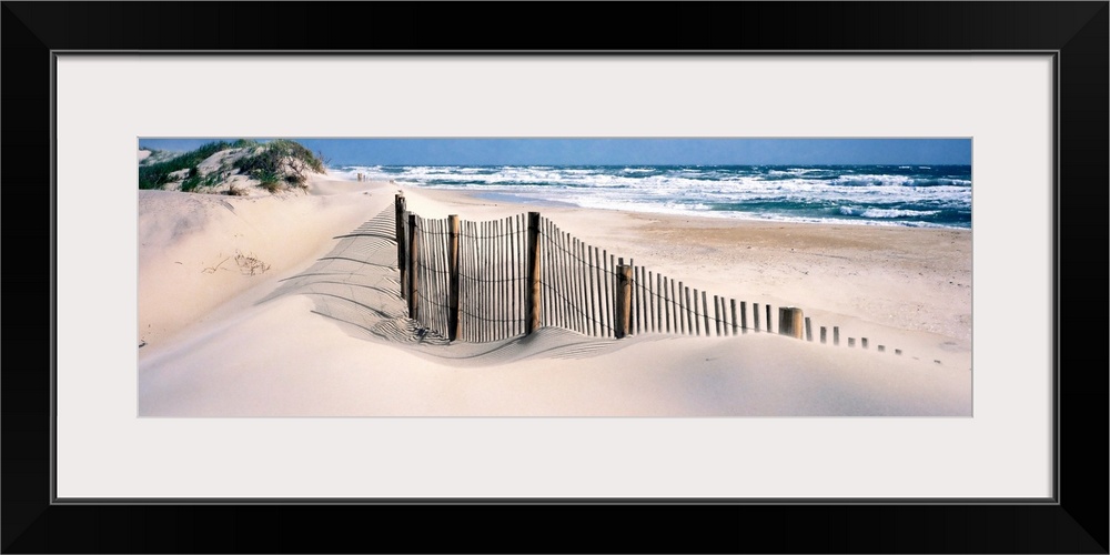 A wooden fence separates sand dunes from the Atlantic Ocean in this panoramic image.