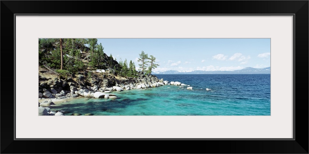 Panoramic photograph on a large wall hanging of the rocky North Shore of Lake Tahoe, the hillside covered in trees, surrou...