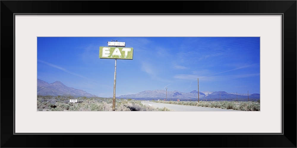 A large sign with the word Eat stands alone in the desert with mountainous terrain lining the background.