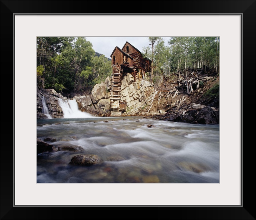 Photograph of old log cabin sitting on top of rocky hill with rushing stream below.