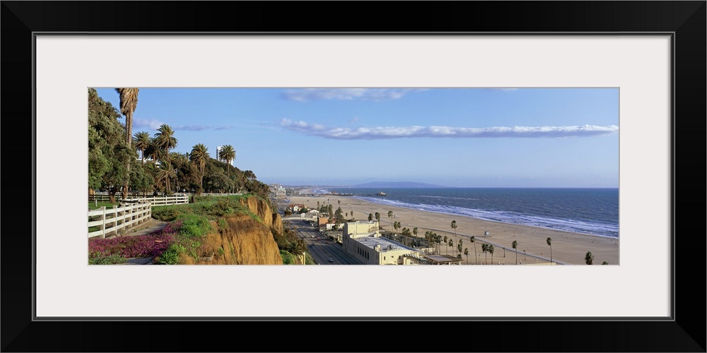 Panoramic photograph of cliff overlooking shoreline filled with buildings and palm trees under a cloudy sky.