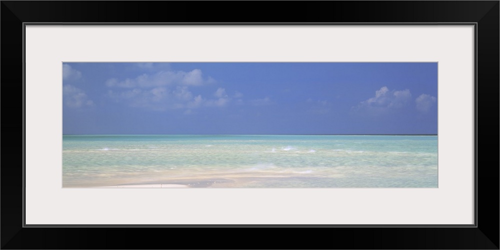 Panoramic canvas photo of a clear ocean meeting a sandy beach.