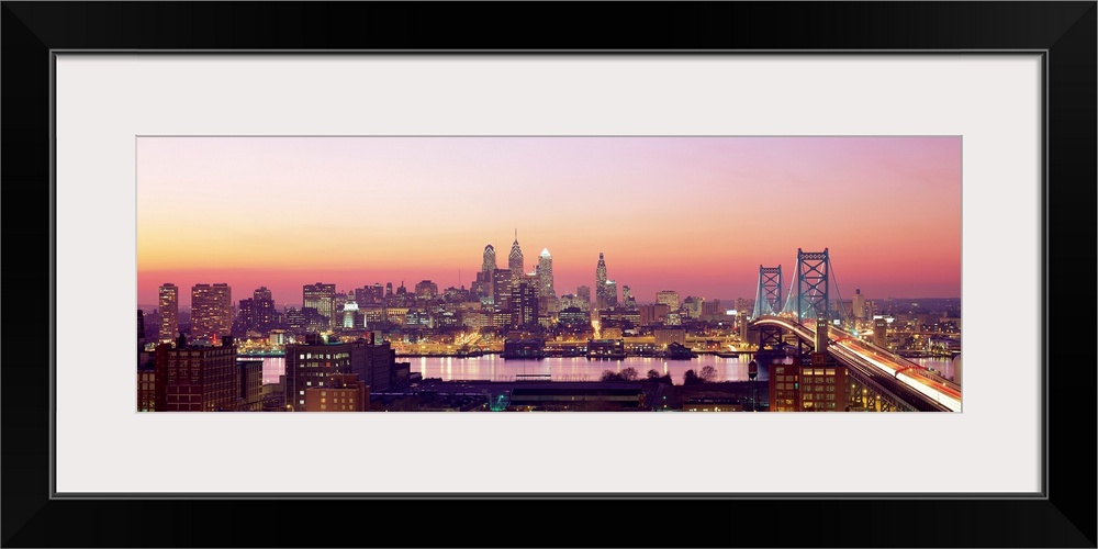 Panoramic photograph displays the busy skyline and Benjamin Franklin bridge in Philadelphia, Pennsylvania at twilight.  Th...
