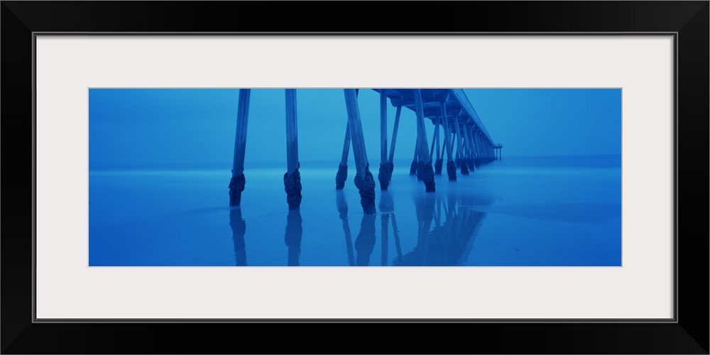 Photograph taken underneath a long pier that stretches far out into the ocean.