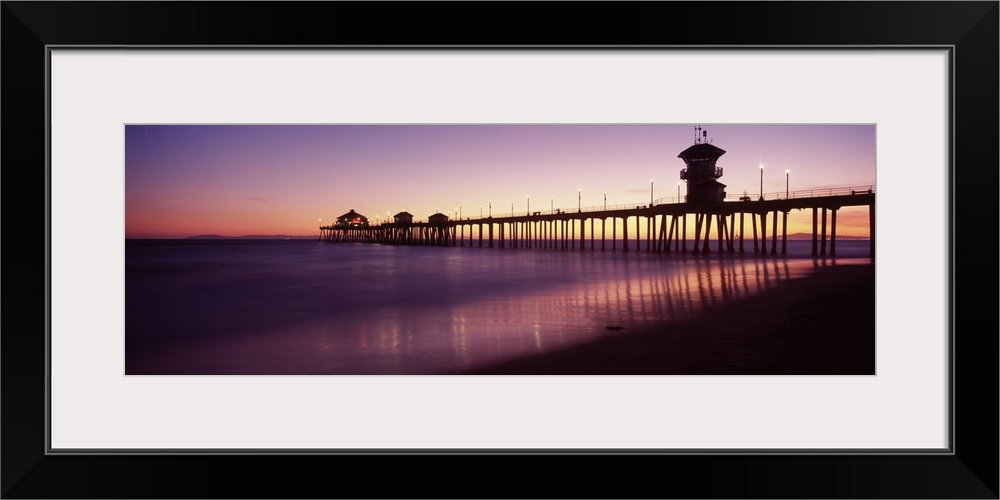 Panoramic photograph composed of a large dock extending into the Pacific Ocean while the waves slowly make their way to th...