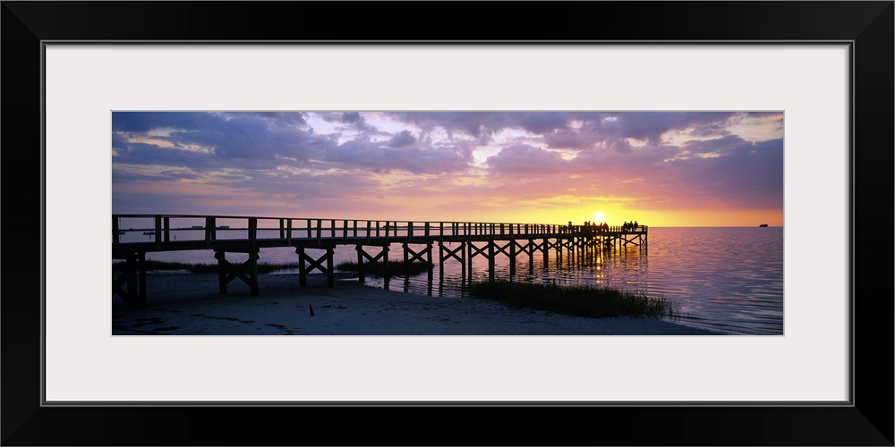 Oversized, panoramic photograph of the pier extending into the water, toward the setting sun at Crystal Beach, Florida.