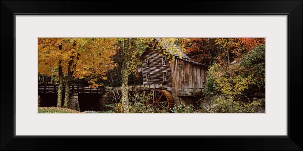 Wide angle view of an old mill surrounded by trees and foliage in the autumn. A small bridge is shown just to the left of ...