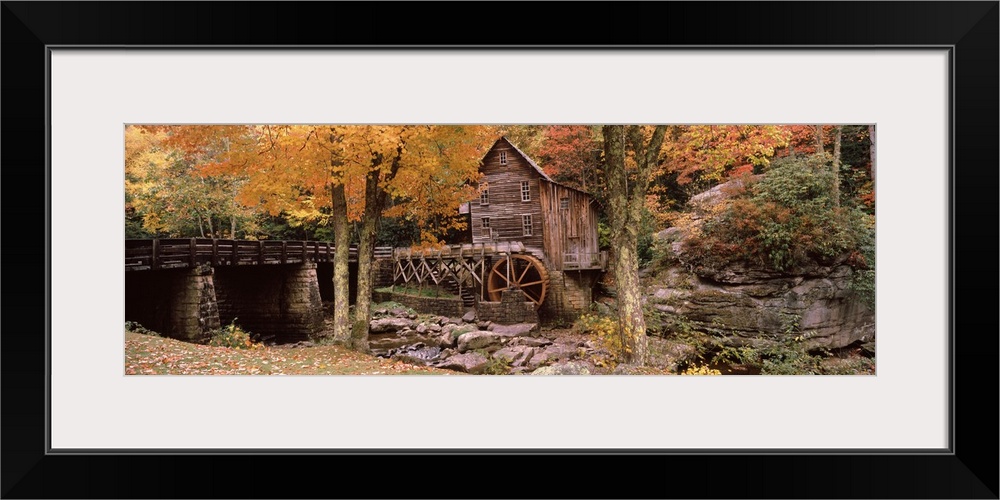 Panoramic photograph of old stone bridge leading to water mill located in a fall forest.