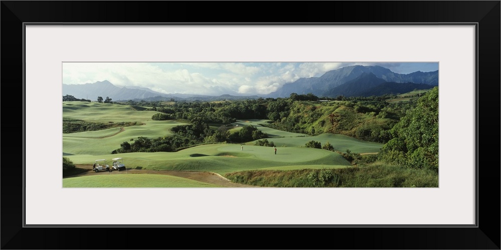 Panoramic picture of rolling hills of a golf course nestled in the Hawaiian mountains.