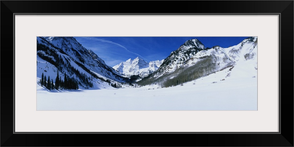 Panoramic photograph of snow covered mountains and trees under a cloudy sky.