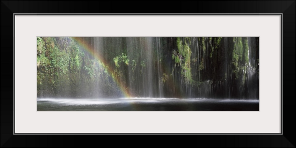 Panoramic photograph of a double rainbow shown in front of a wide waterfall.