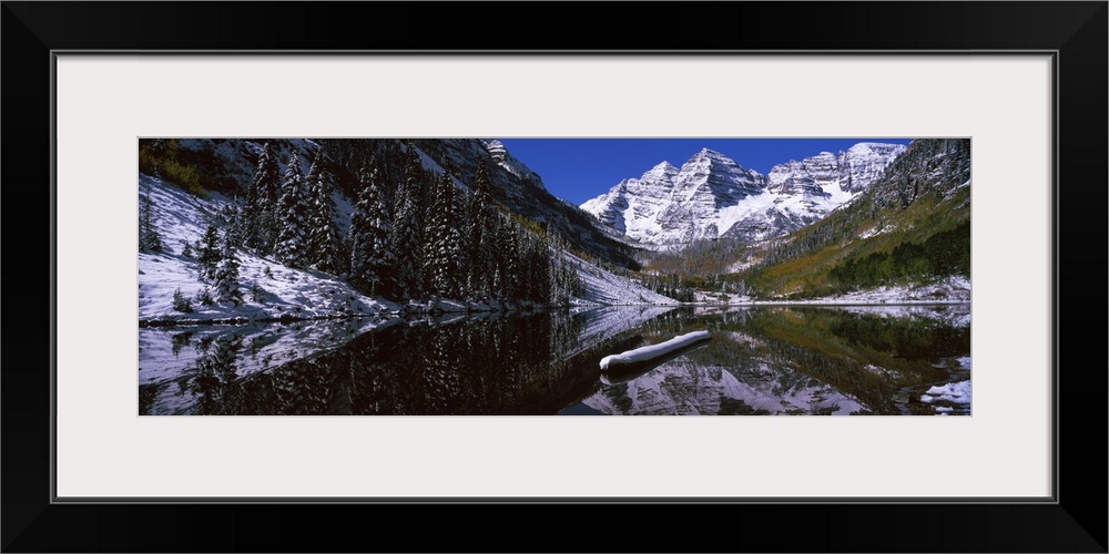 View from the water in a Rocky Mountain valley, the snowcapped mountain range reflected in the still water.