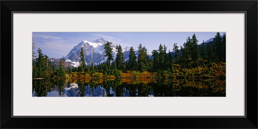 Pine trees and a snow covered mountain reflect perfectly into the lake that sits in front of them.