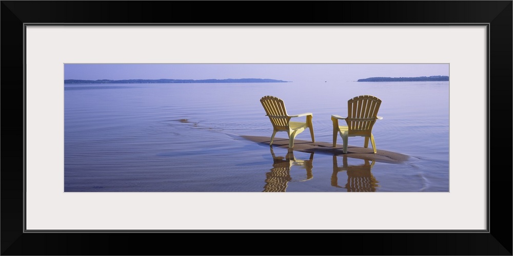 Panoramic photograph of two beach chairs sitting on top of sand bar with land in the far distance.