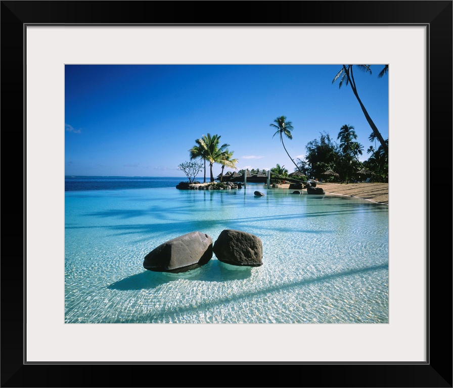 Large landscape artwork for a living room or office of clear water ripples around rocks on a tropical beach lined by palm ...