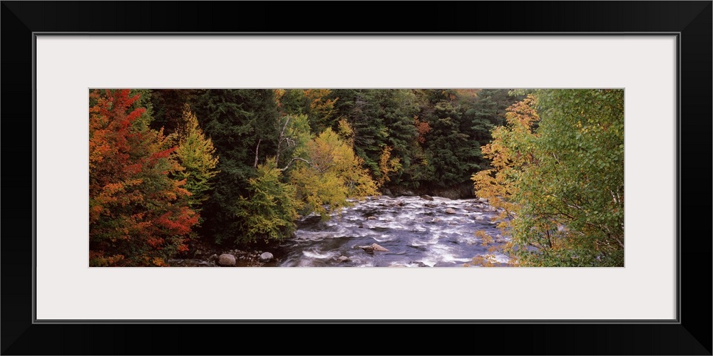 This decorative landscape wall art is a panoramic photograph of a rock filled river riffling through an autumn woodland.