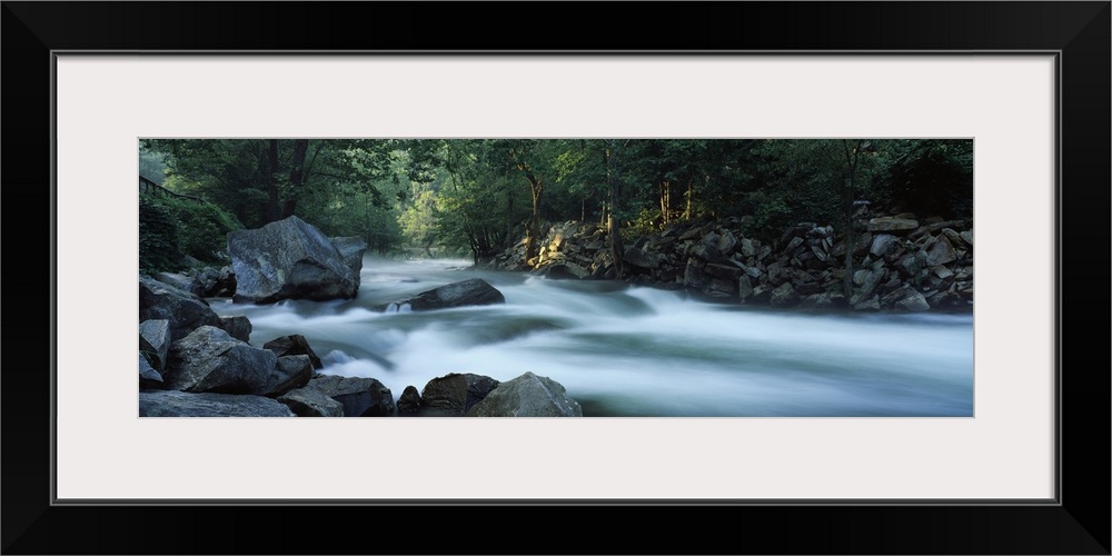 Panoramic photograph of rocky stream lined with forest.