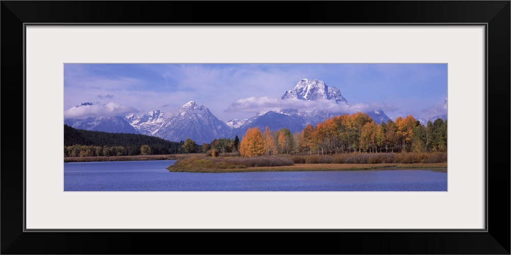 Mountainous terrain with clouds hovering near the peaks is photographed from across a large body of water.