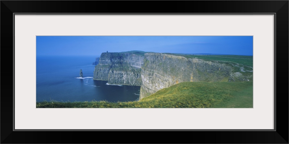 Wide angle photograph of curving, large rock formations of the Cliffs of Moher, leading into the water in County Clare, th...