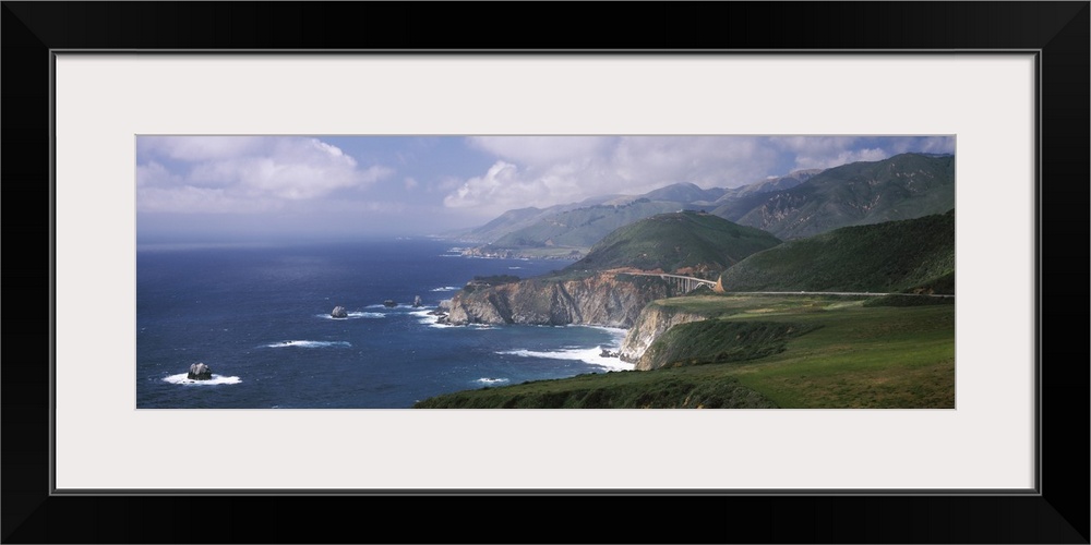 Large panoramic view of rock formations in the pacific ocean and immense mountains along the California coast.