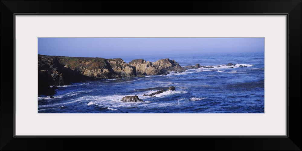 Wide angle photograph of the bright blue waters of Big Sur lapping around large rock formations near Garrapata State Beach...