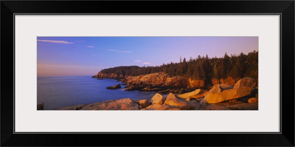 Wide angle photograph of the rocky shoreline, surrounded by trees at sunset, in Acadia National Park, Maine.