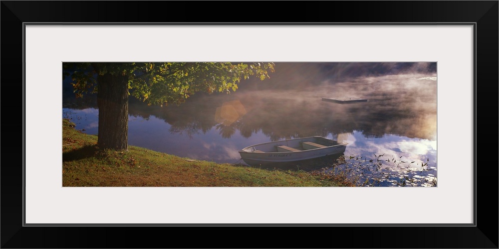 Small boat resting on the shore of a misty lake next to a sturdy tree, the surrounding forest reflected in the water.