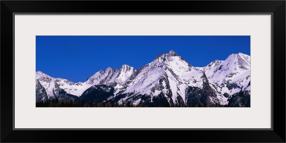 Snow capped Mountain range protrudes in to the brilliant blue sky in Colorado.