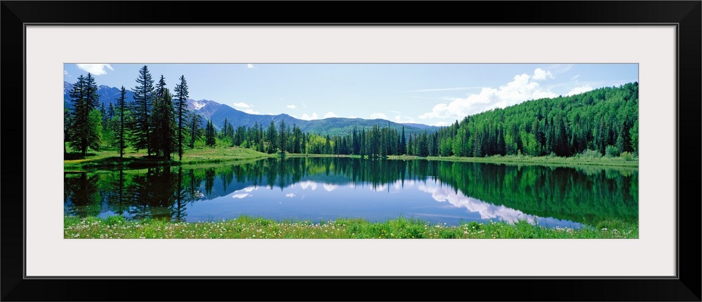 The still waters of a Colorado lake reflect the trees and clouds in this panoramic landscape photograph.