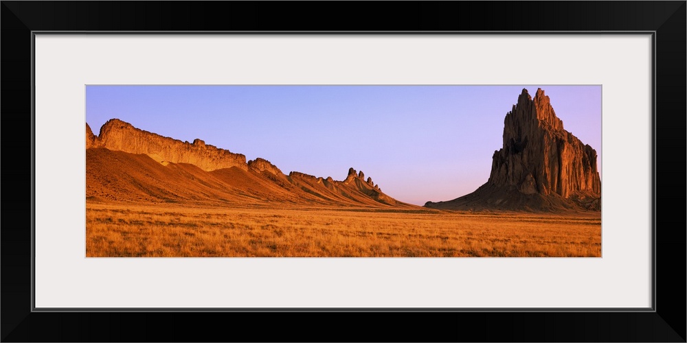 Ship Rock mountain is skewed to the right side of this panoramic piece with vast desert terrain to the left while the sun ...