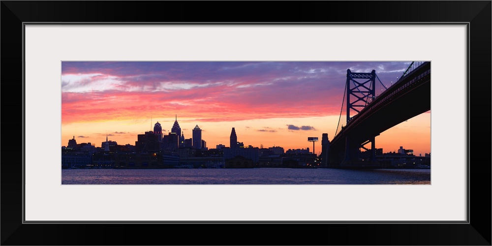 View from the shoreline under the bridge of pastel-colored clouds over the city skyline at dusk.