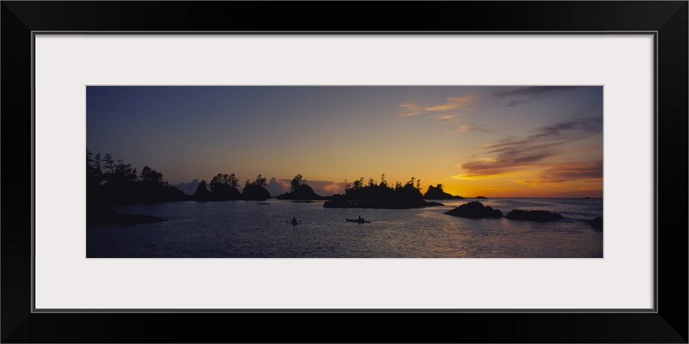 Tiny islands and boats on the water are silhouetted by the sunset that has gone below the horizon.